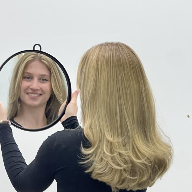 A client looking at her light blonde layered balayage in a hand mirror