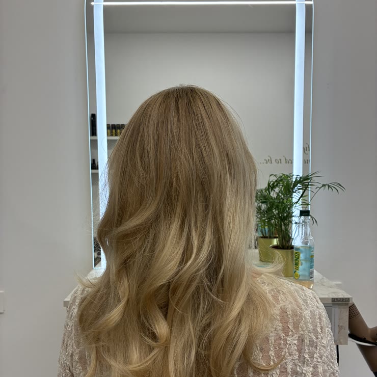 Blonde balayage with waves in front of the lit salon mirror